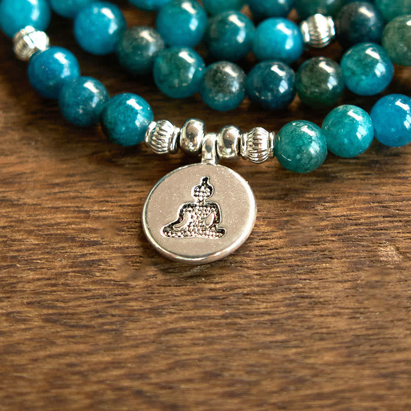 108 Mala Apatite Bracelet - macro close-up of silver Buddha meditation charm on teal beads, wood
