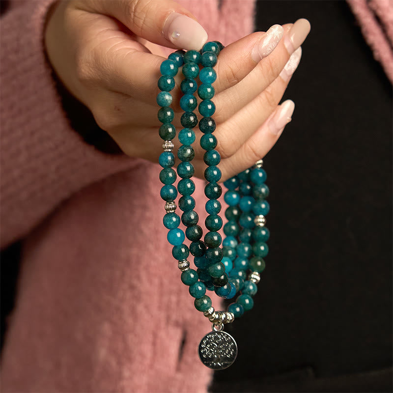 108 Mala Apatite Bracelet - hand holding teal bead strands with Tree of Life pendant, pink sweater