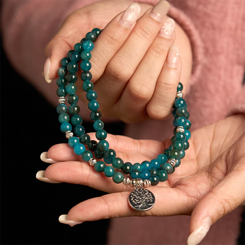 108 Mala Apatite Bracelet - two hands displaying teal beads with Tree of Life charm, French manicure