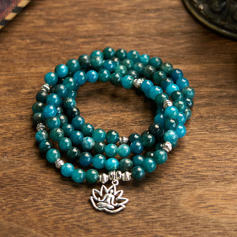 108 Mala Apatite Bracelet - coiled teal beads with Lotus Buddha charm on wooden table, zen jewelry