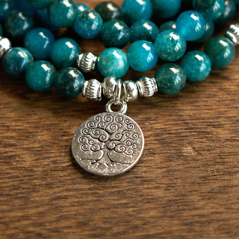108 Mala Apatite Bracelet - macro close-up of silver Tree of Life charm on teal beads, wood surface