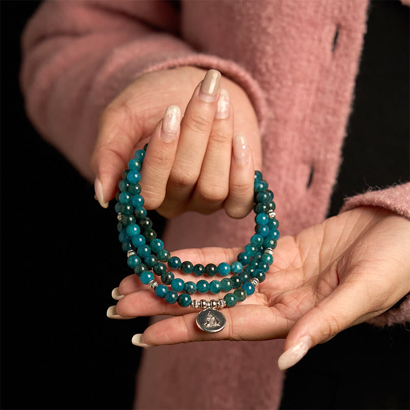 108 Mala Apatite Bracelet - two hands displaying teal beads with Buddha medallion, black background