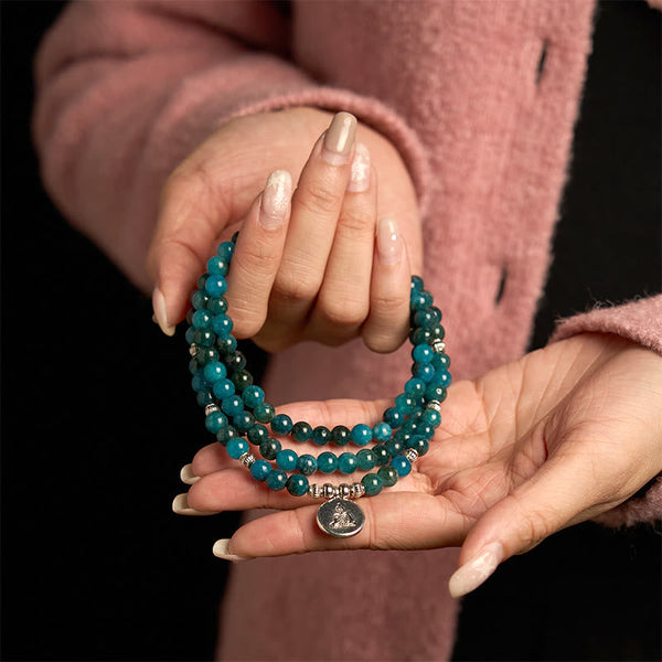 108 Mala Apatite Bracelet - two hands displaying teal beads with Buddha medallion, black background