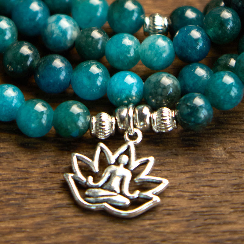 108 Mala Apatite Bracelet - macro close-up of silver lotus Buddha charm on teal beads, wood surface