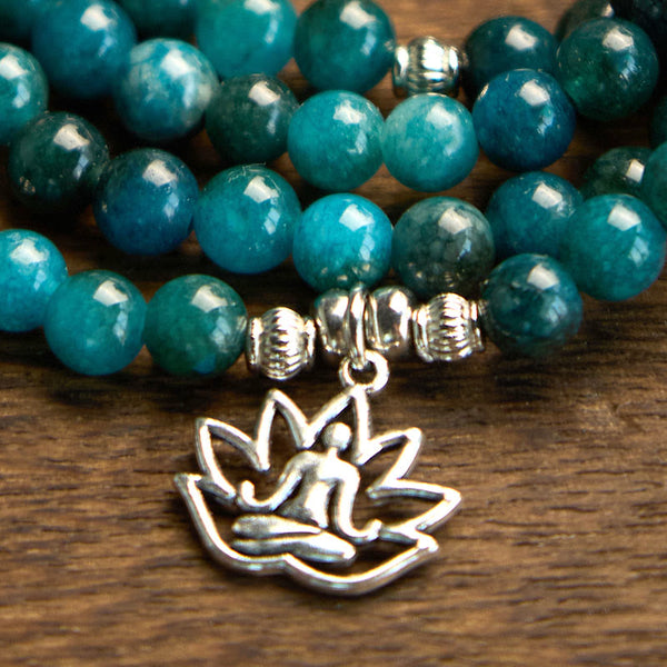 108 Mala Apatite Bracelet - macro close-up of silver lotus Buddha charm on teal beads, wood surface