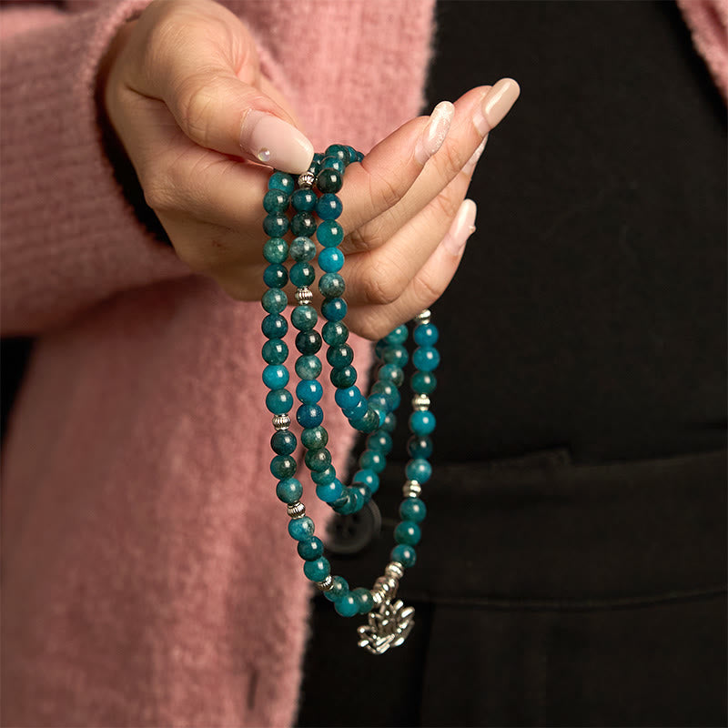 108 Mala Apatite Bracelet - hand holding teal bead strands with lotus flower charm, dark background
