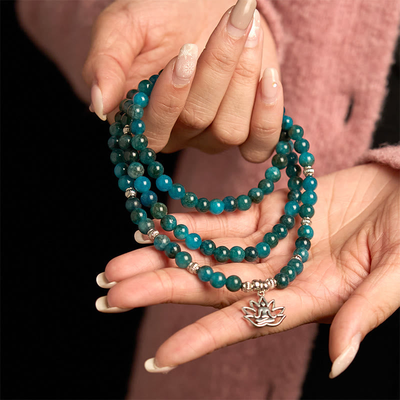 108 Mala Apatite Bracelet - two hands displaying teal beads with lotus Buddha charm, black background