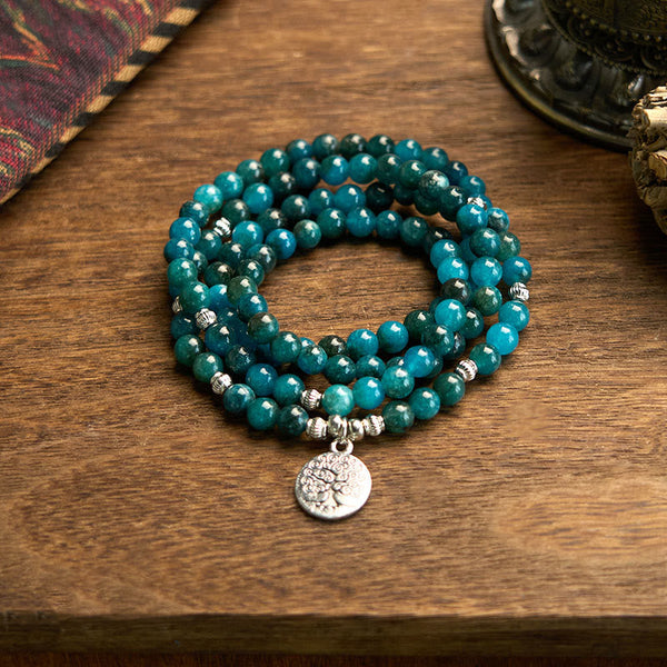 108 Mala Apatite Bracelet - coiled teal beads with Tree of Life charm on wooden table, yoga jewelry