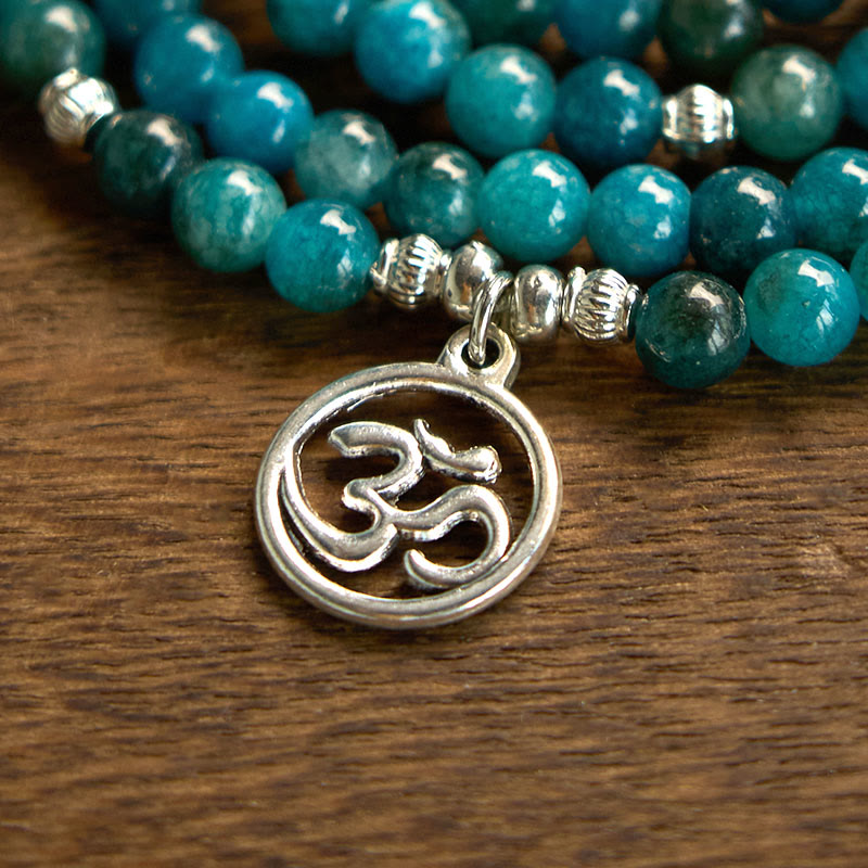 108 Mala Apatite Bracelet - macro close-up of silver Om charm on teal gemstone beads, wood surface