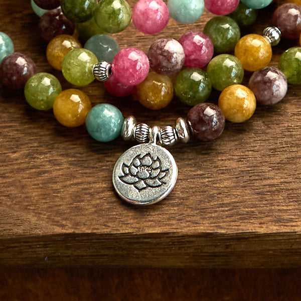 108 Mala Tourmaline Lotus Wisdom Bracelet - silver lotus charm close-up on wood grain, Healing