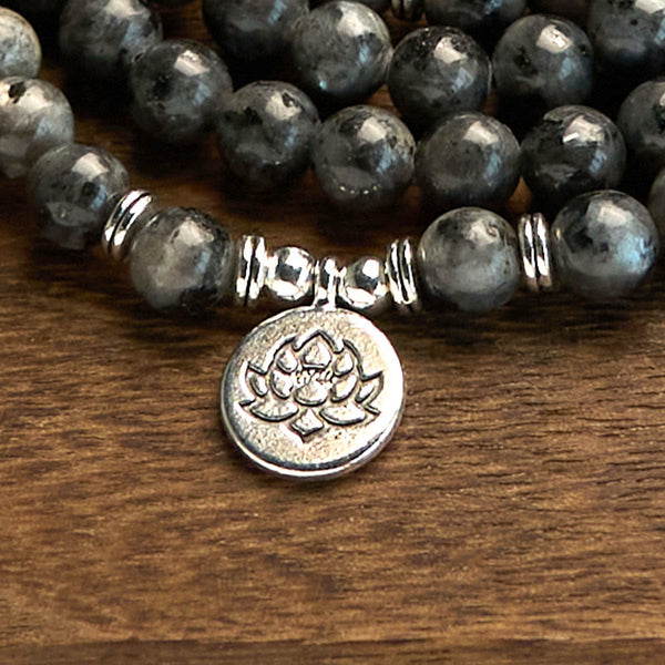 108 Mala Black Glitter Stone Lotus Bracelet - diagonal strands on warm wood, silver lotus focus, striking resilience