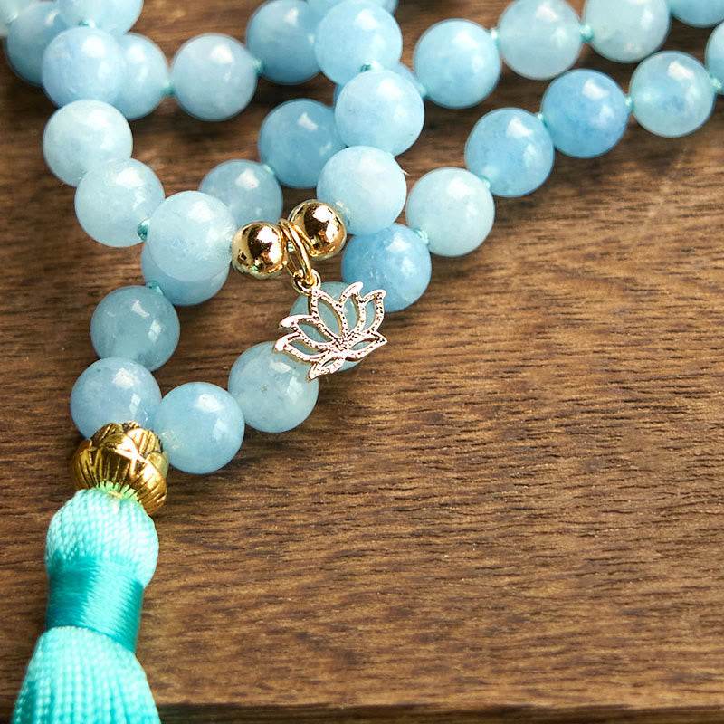 108 Mala Aquamarine Lotus Healing Bracelet – close-up gold lotus guru bead and turquoise tassel on wood grain, Clarity