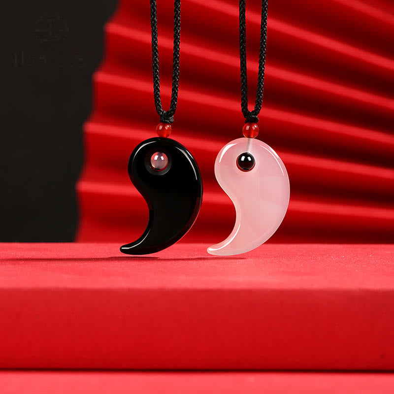 Black Onyx White Agate Yin Yang Necklace - Two matching yin-yang pendant necklaces hanging side by side on deep red fabric...