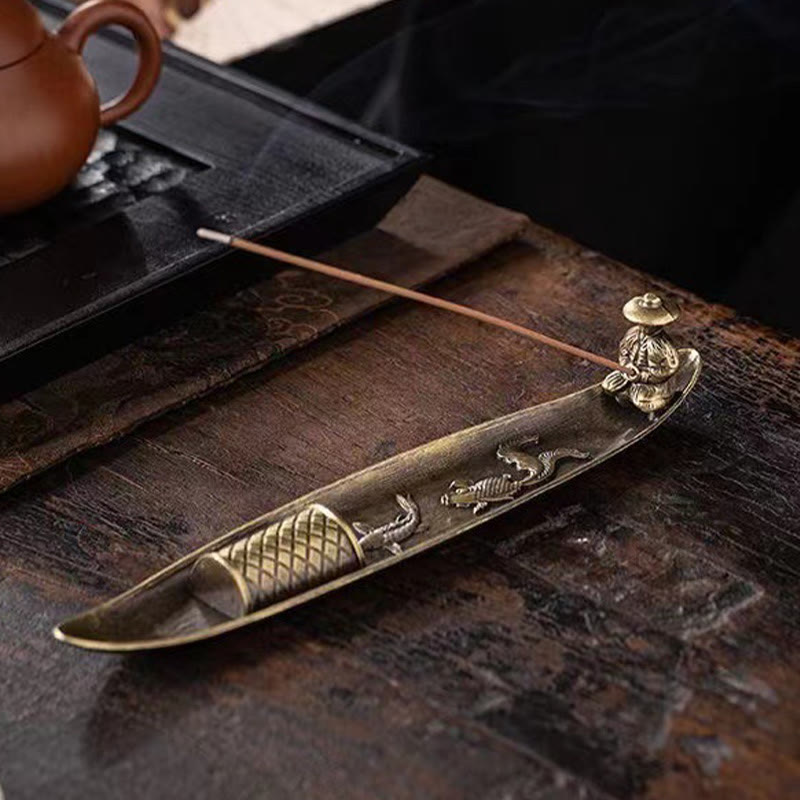 Koi Fish Boat Incense Burner - three-quarter view with fisherman, fish reliefs, and teapot on dark wood
