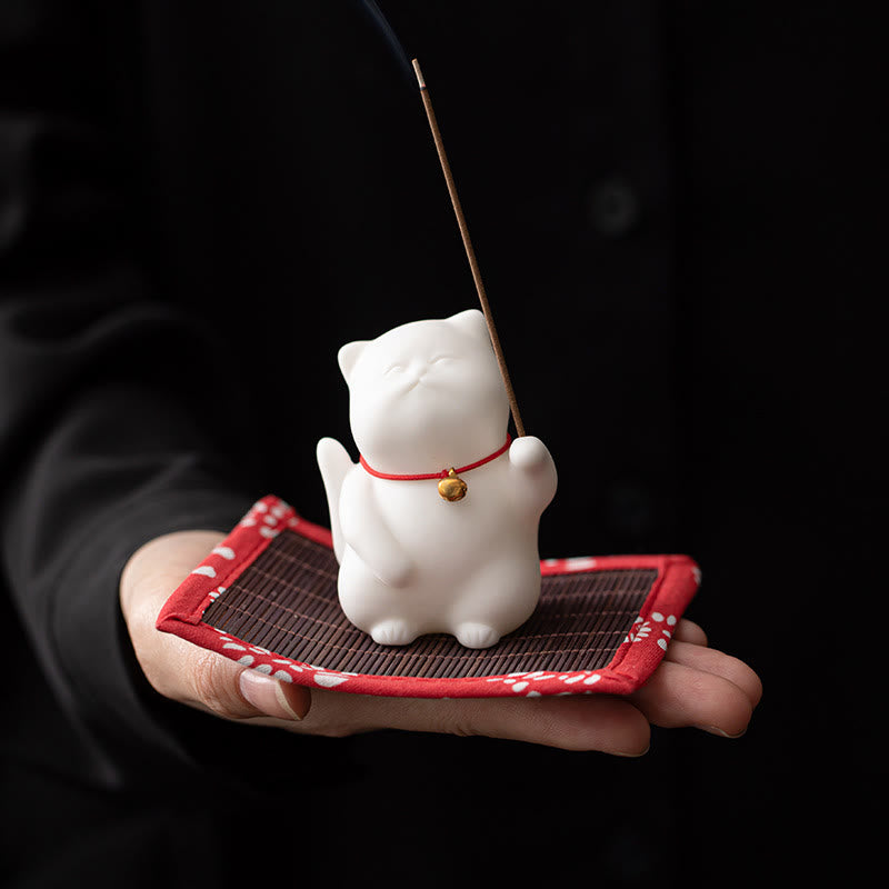 Cat Bell Ceramic Incense Burner – White cat held in palm on floral mat, burning incense stick, ceramic incense holder