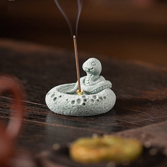Chinese Zodiac Sandstone Incense Burner – coiled snake figurine with incense smoke, dark wood bokeh, sage green stone