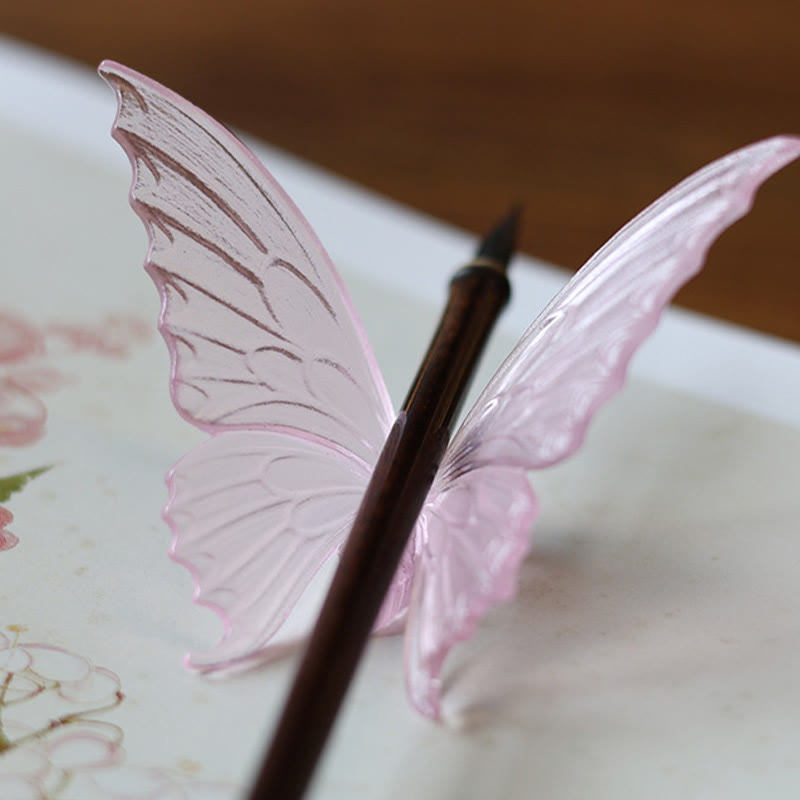 Butterfly Liuli Glass Incense Burner - Pink translucent butterfly cradling a wooden pen on floral paper, desk accessory
