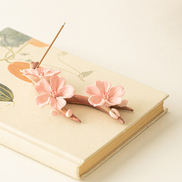 Plum Blossom Incense Burner – Pink cherry blossom ceramic holder on botanical book, artisan decor