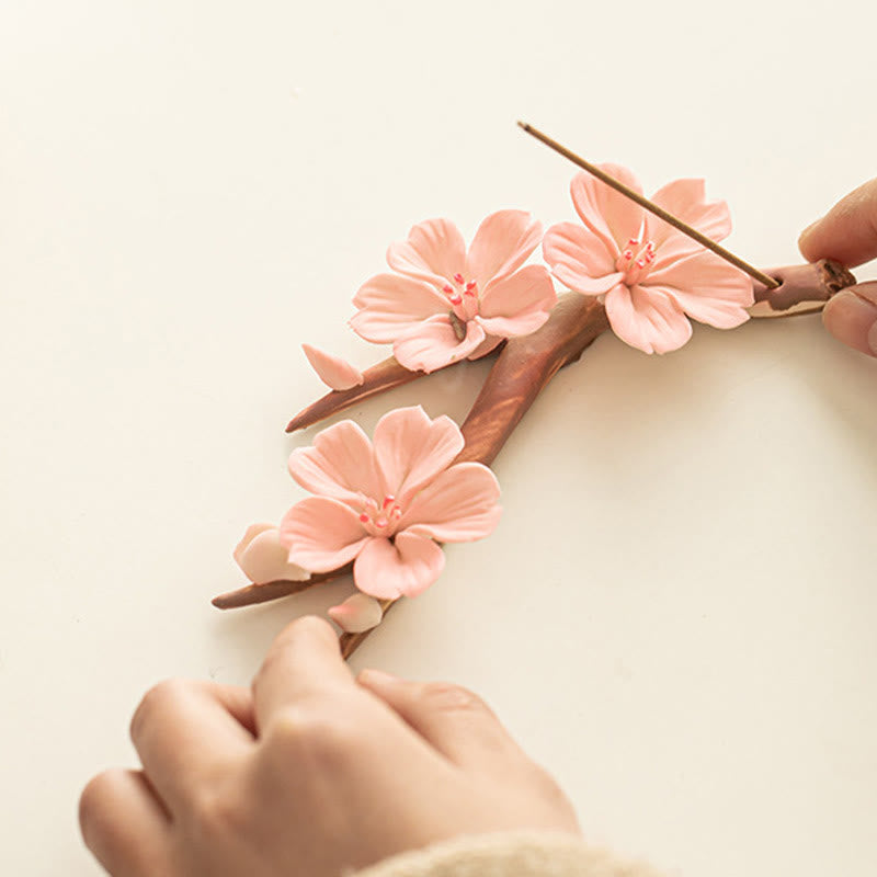 Plum Blossom Incense Burner – Hands inserting incense into pink cherry blossom flowers, ceramic holder