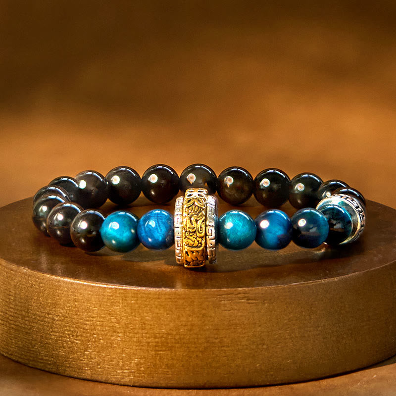 Om Mani Padme Hum Bracelet – Black and blue beaded bracelet with gold charm on wooden stand, protection bracelet