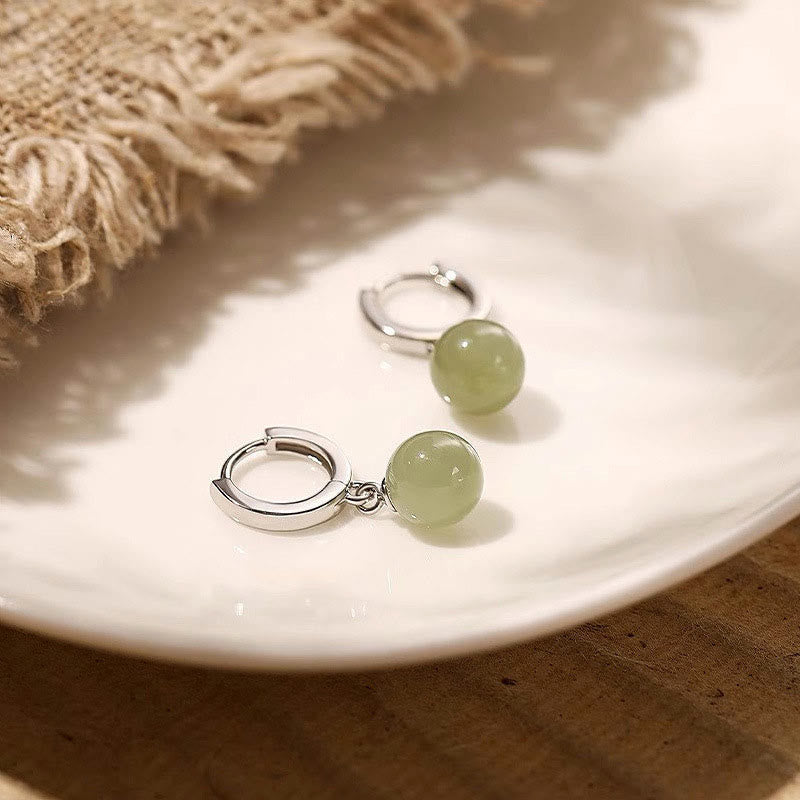 Round Jade Bead Prosperity Earrings – silver hoops with celadon jade drops on white ceramic dish with linen texture, elevated angle