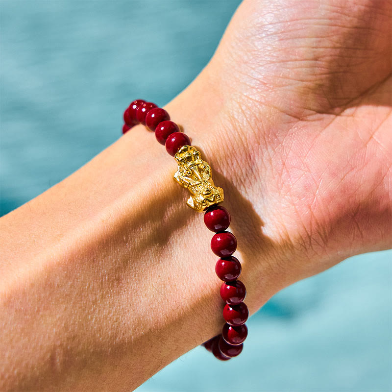 Natural Cinnabar Beads PiXiu Blessing Bracelet – wrist view with gold PiXiu and red beads against blue water, spiritual jewelry