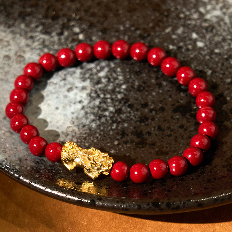 Natural Cinnabar Beads PiXiu Blessing Bracelet – gold PiXiu with red cinnabar beads on dark ceramic plate, good luck jewelry