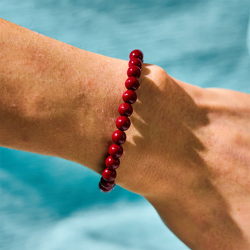 Natural Cinnabar Beads PiXiu Blessing Bracelet – gold PiXiu with red cinnabar beads on warm golden wood surface, prosperity