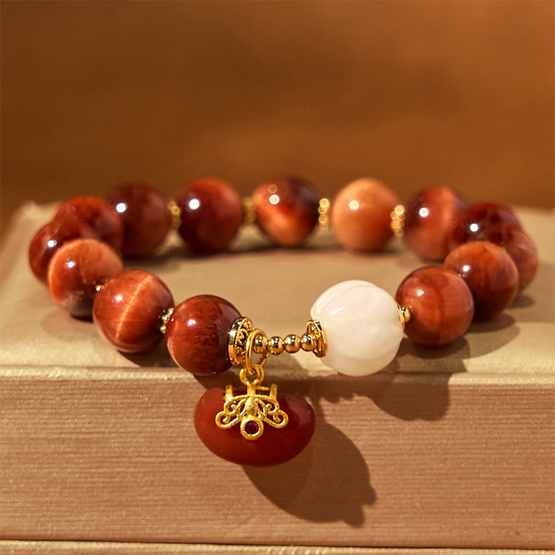 Natural Red Tiger Eye Pumpkin Calm Bracelet – Red tiger eye bracelet with gold charm on stacked books, warm lighting