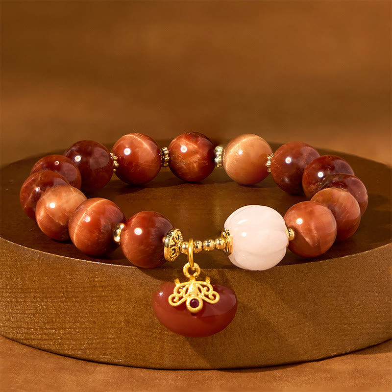 Red Tiger Eye Pumpkin Bracelet – Red tiger eye beads with white pumpkin on dark wood pedestal, warm golden lighting
