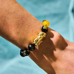 Obsidian PiXiu Five Gods Bracelet – Side view on wrist with black obsidian beads and gold PiXiu, turquoise water background