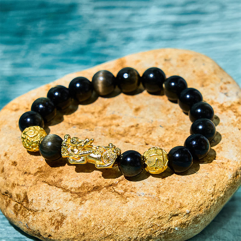 Gold Sheen Obsidian PiXiu Bracelet – Black obsidian beads with gold PiXiu and engraved gold beads on stone, water background