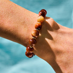 Red Tiger Eye Pumpkin Bracelet – Side view on wrist showing red tiger eye beads and gold spacers, water background