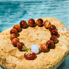 Red Tiger Eye Pumpkin Bracelet – Red tiger eye beads with white pumpkin and red charm on stone, turquoise water background