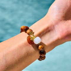 Red Tiger Eye Pumpkin Bracelet – Worn on wrist with red tiger eye beads, white pumpkin and gold charm, water background