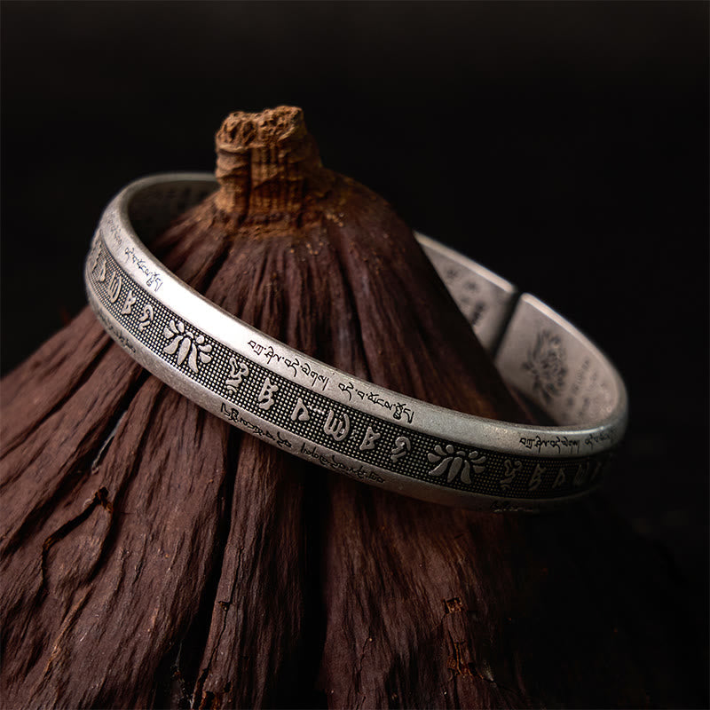 Lotus Mantra Cuff Bracelet – Full view on natural wood prop, Tibetan sacred text and lotus carvings, silver jewelry