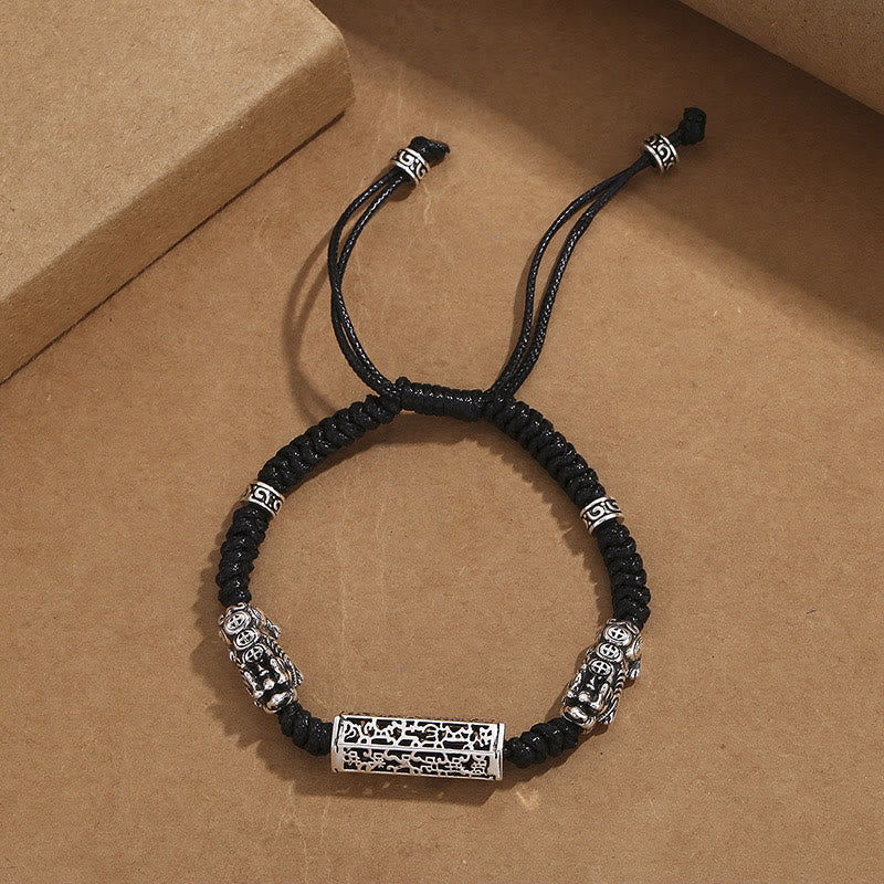 Tibetan PiXiu Bracelet – Black cord bracelet with silver PiXiu and copper Om Mani Padme Hum cylinder on gray surface