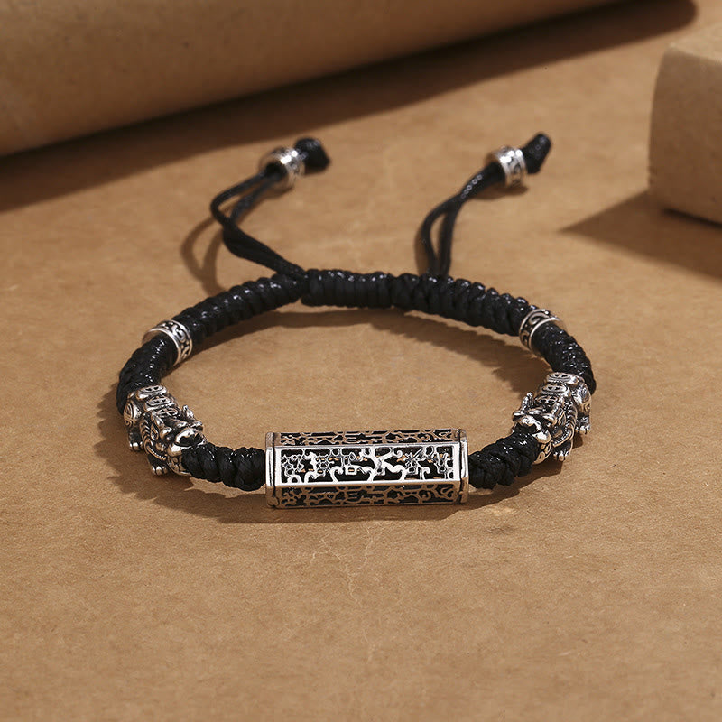 Tibetan PiXiu Bracelet – Black braided cord with silver PiXiu and copper Om Mani Padme Hum cylinder on brown paper
