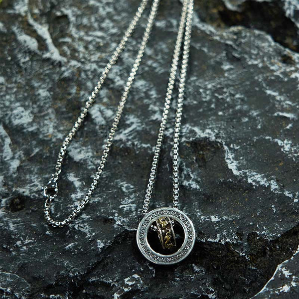 Double Ring PiXiu Necklace – Silver circular pendant with golden PiXiu on chain over dark textured volcanic rock