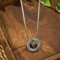 Double Ring PiXiu Necklace – Silver peace buckle pendant with golden PiXiu on wooden surface with green leaves