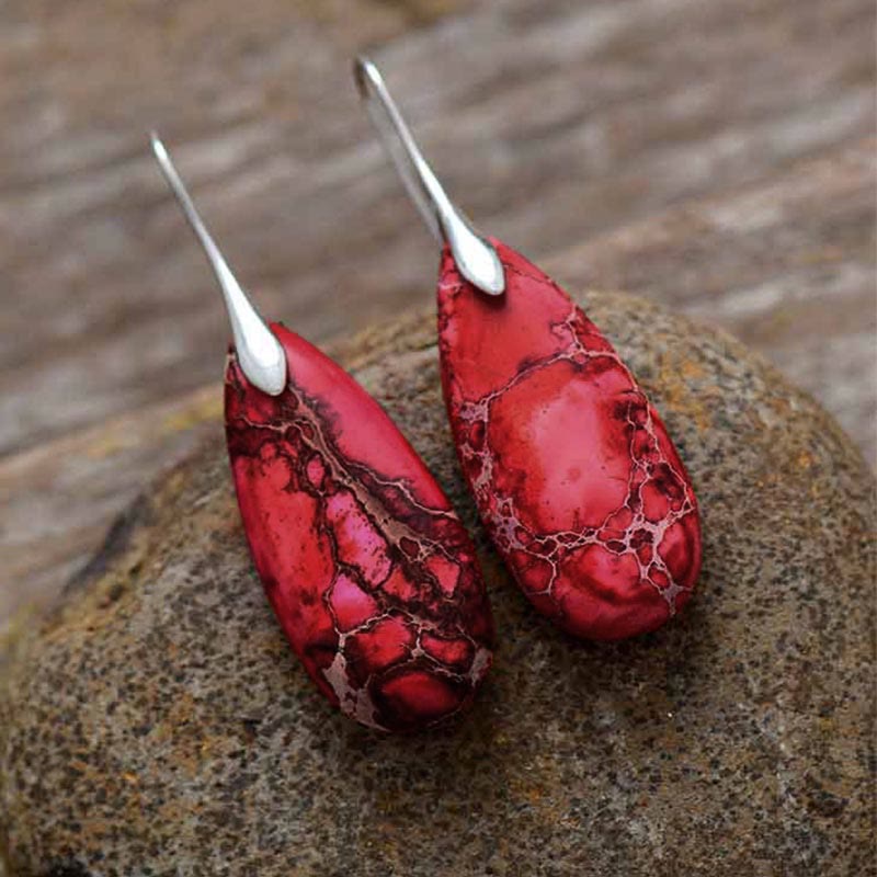 Emperor Stone Healing Crystal Earrings – Red teardrop natural stone earrings with dark webbing cracks on rough natural rock with wood background