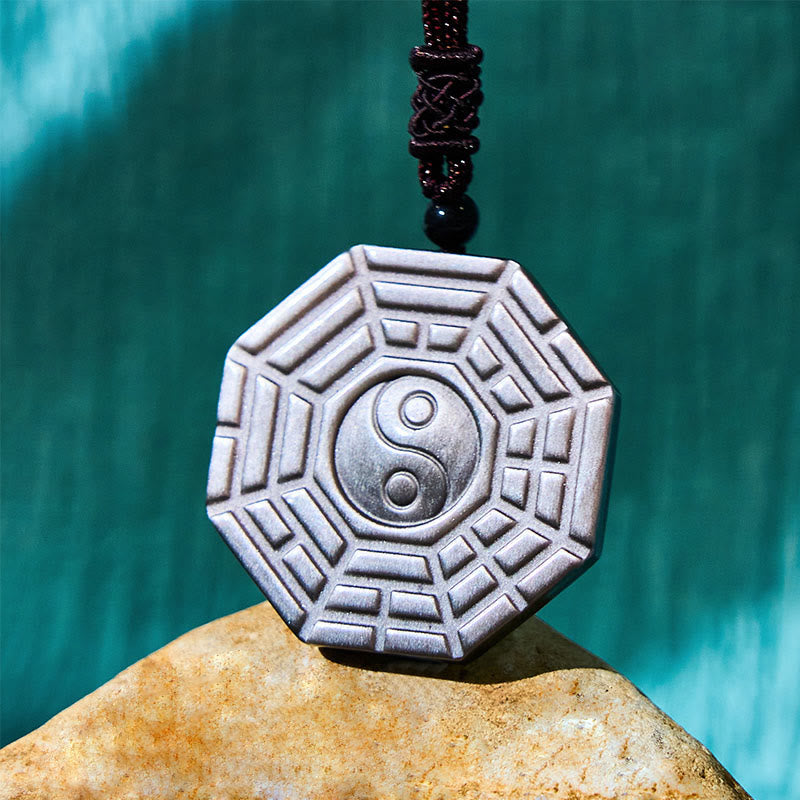 Silver Sheen Obsidian Bagua Yin Yang Pendant on natural stone with teal bokeh, zen necklace