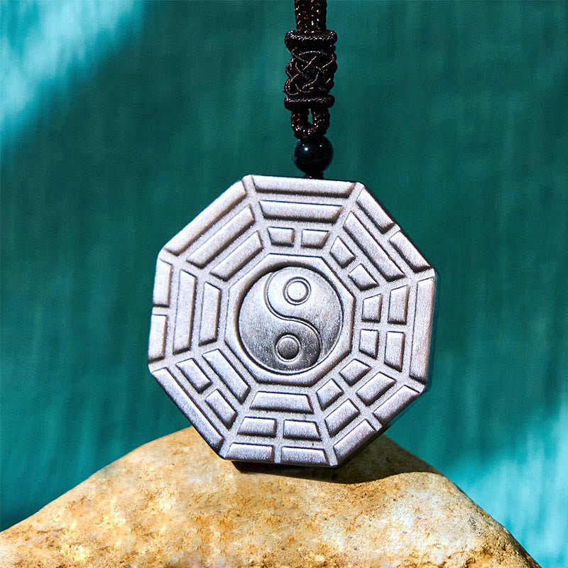 Silver Sheen Obsidian Bagua Yin Yang Pendant on smooth stone with teal gradient, obsidian amulet