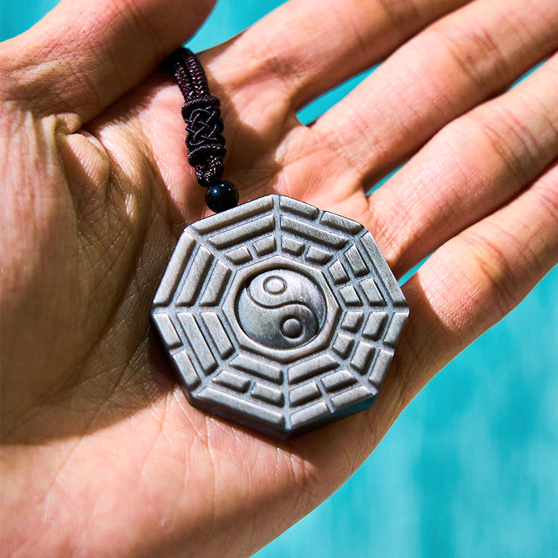 Silver Sheen Obsidian Bagua Yin Yang Pendant in hand with turquoise backdrop, braided cord detail