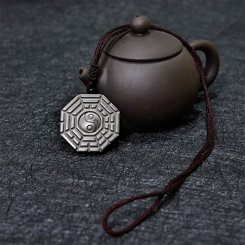 Silver Sheen Obsidian Bagua Yin Yang Pendant beside traditional teapot on slate, spiritual jewelry decor