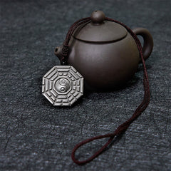 Silver Sheen Obsidian Bagua Yin Yang Pendant beside traditional teapot on slate, spiritual jewelry decor