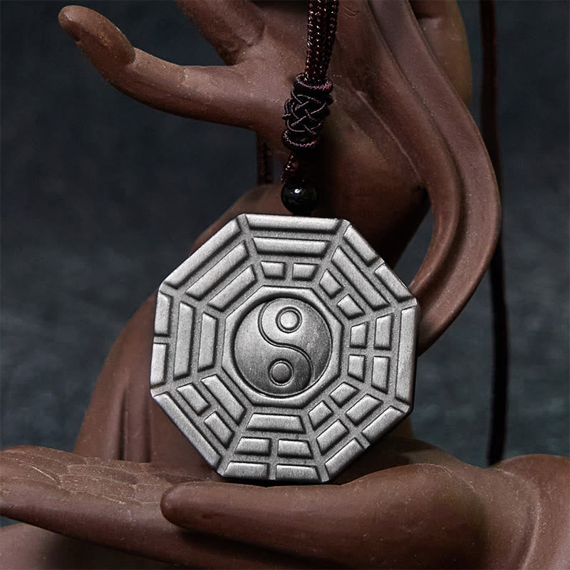 Silver Sheen Obsidian Bagua Yin Yang Pendant cradled by Buddha hand sculpture, meditation jewelry