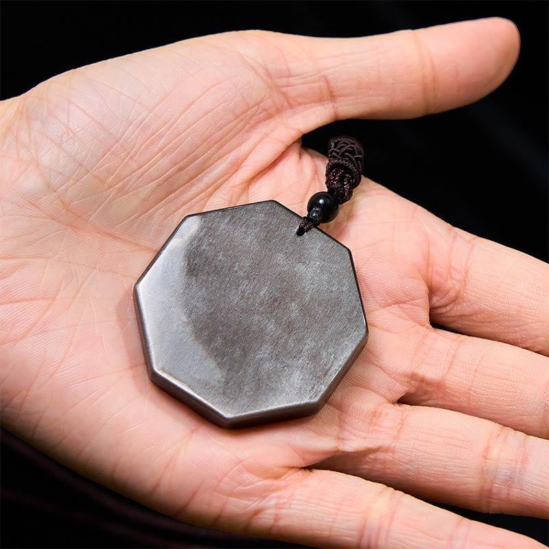 Silver Sheen Obsidian Bagua Yin Yang Pendant held in palm on black background, hand size reference
