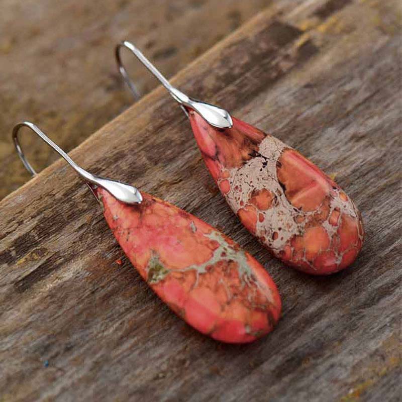 Emperor Stone Healing Crystal Earrings – Orange red teardrop jasper earrings with white vein webbing and silver hooks on weathered wood surface