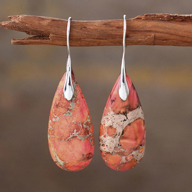 Emperor Stone Healing Crystal Earrings – Coral pink salmon red teardrop earrings with white cream matrix patterns hanging on natural driftwood branch